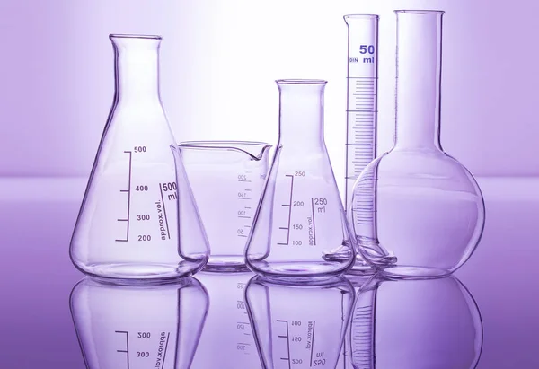 Chemiegläser isoliert auf reflektierender Oberfläche im violetten Hintergrund — Stockfoto