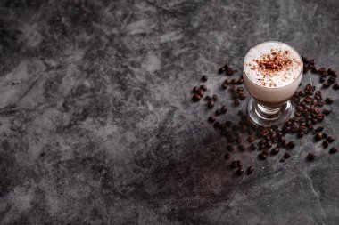 Siyah arka planda bir fincan kapuçino. Kavrulmuş kahve çekirdekleri.