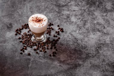 Siyah arka planda bir fincan kapuçino. Kavrulmuş kahve çekirdekleri.