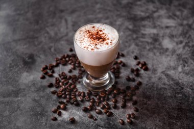 Siyah arka planda bir fincan kapuçino. Kavrulmuş kahve çekirdekleri.