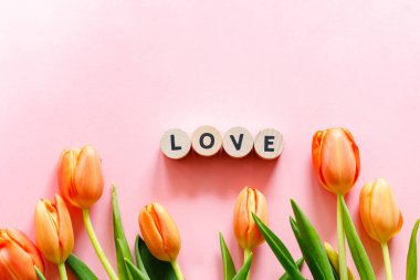 Pembe arka planda turuncu laleler ve küp şeklinde aşk sözcükleri.