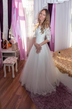 Gelinlik giymiş genç bir gelin pencerenin yanındaki odada düğün töreninin başlamasını bekliyor..