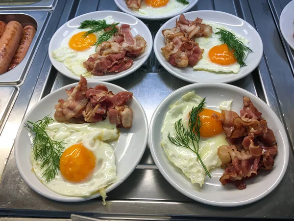 Fried eggs with bacon and a sprig of dill on a white plate, ready to serve.