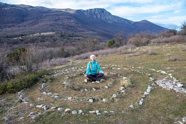 Yetişkin bir kadın, Paragilmen Dağı 'nın tepesinde taşlardan yapılmış bir sarmalın ortasında yoga yapıyor. Gücün esrarengiz yeri. Yaşam biçimi.