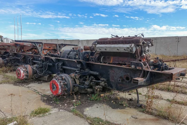 Terk edilmiş paslı bir çerçeve ve eski bir savaş aracının şanzımanı. Tekerleksiz, açık alanda duruyor..