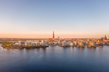 Rostock şehrinin panoraması. Nehir savaşı sırasında hava manzarası, gün doğumunda gökyüzü.