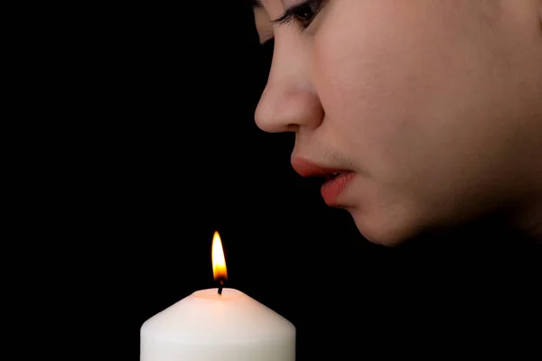 Mujer joven soplando una vela en el fondo negro — Foto de Stock