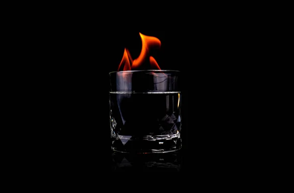 Glass with vodca and fire flame on black background — 스톡 사진