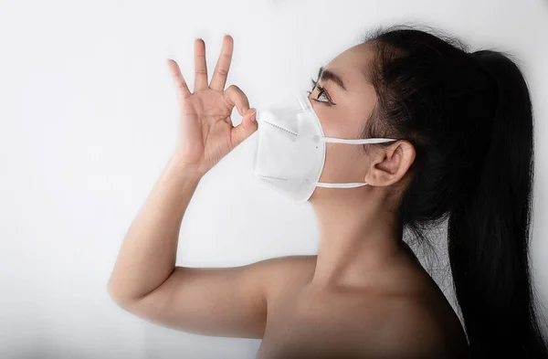 Close up of a woman putting on a respirator N95 mask to protect from airborne respiratory diseases as the flu covid-19 corona PM2.5 dust and smog, Female thumbs-up gesture with hand showing o.k sign