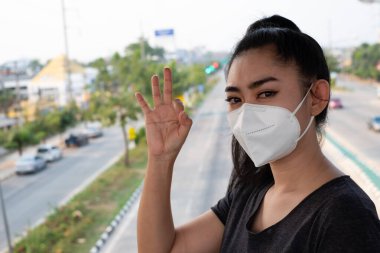 Hava yoluyla bulaşan solunum hastalıklarından korumak için N95 maskesi takan bir kadına yakından bakın. Grip vid-19 koronavirüs ebola Pm2.5 tozu ve yoldaki dumanlar arka planda patlamış.