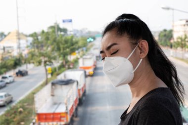 Hava yoluyla bulaşan solunum hastalıklarından korumak için N95 maskesi takan bir kadına yakından bakın. Grip vid-19 koronavirüs ebola Pm2.5 tozu ve yoldaki dumanlar arka planda patlamış.
