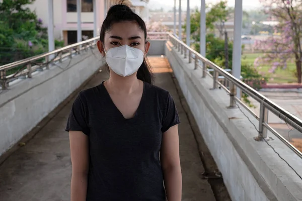 Hava yoluyla bulaşan solunum hastalıklarından korumak için N95 maskesi takan bir kadına yakından bakın. Grip vid-19 koronavirüs ebola Pm2.5 tozu ve yoldaki dumanlar arka planda patlamış.