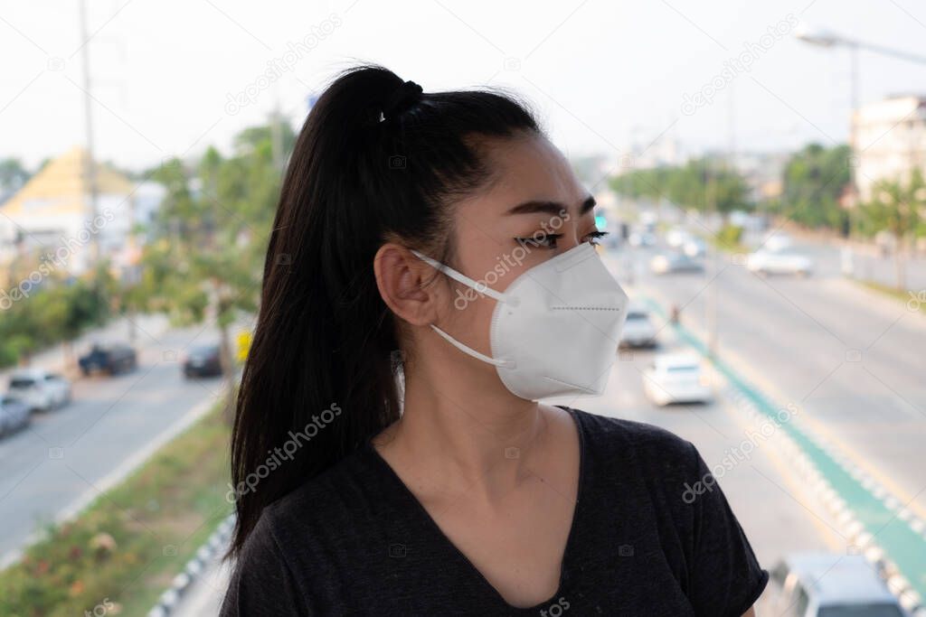Close up of a woman standing putting on a respirator N95 mask to protect from airborne respiratory diseases as the flu covid-19 coronavirus ebola PM2.5 dust and smog on the road burred background