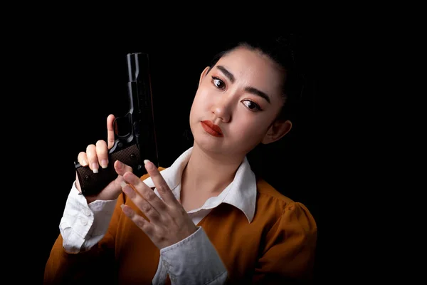 ポートレート美しいですアジアの女性身に着けていますA黄色のスーツ片手黒の背景でピストル銃を保持します 若いですセクシー女の子長い髪とともに拳銃の表情でカメラ 美しいです女性はピストルで立っています — ストック写真