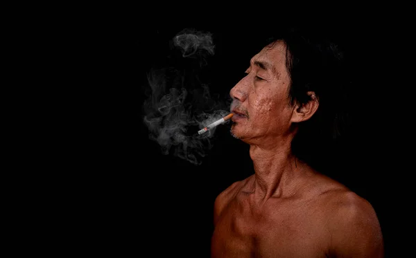 The portrait slim old man was smoking at the black background, Image of cigarette smoke spread in the mouth concept