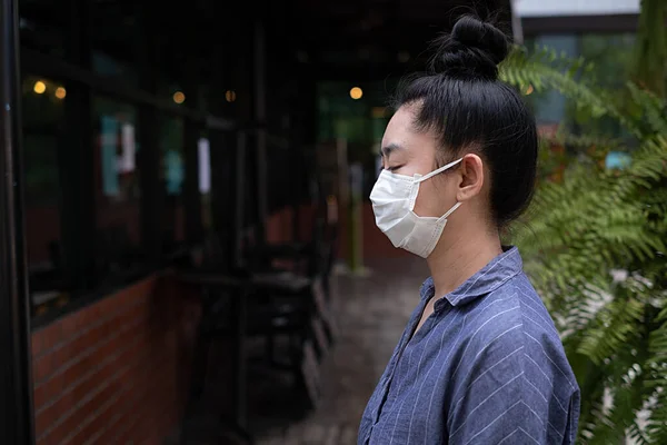 Close up of young Asia woman standing putting on a respirator N95 mask to protect from airborne respiratory diseases as the flu covid-19 coronavirus ebola PM2.5 dust and smog on the road burred background