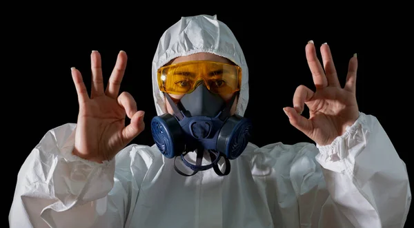 Asia woman o.k hand sign in a chemical protective clothing and antigas mask with glasses black background, Women scientist in safety suit, Safety virus infection concept