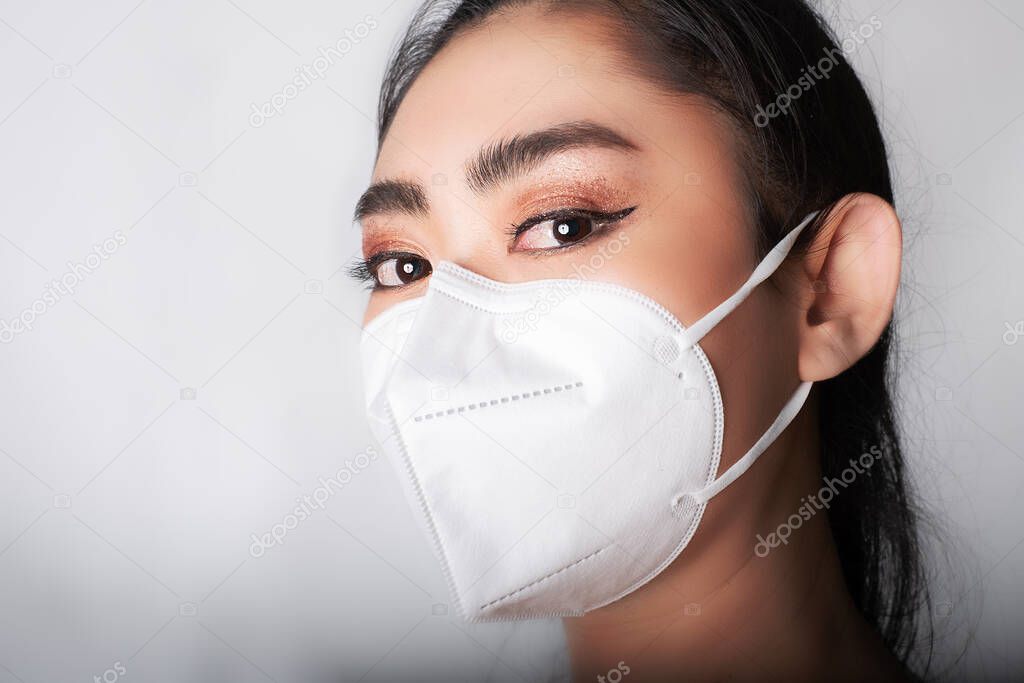Close up of young Asia woman putting on a medical mask n95 to protect from airborne respiratory diseases as the flu covid-19 PM2.5 dust and smog at gray background, Safety virus infection concept