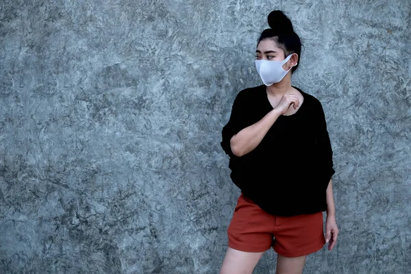 Portrait young Asia woman standing and putting on a fashion mask at concrete wall background with copy space