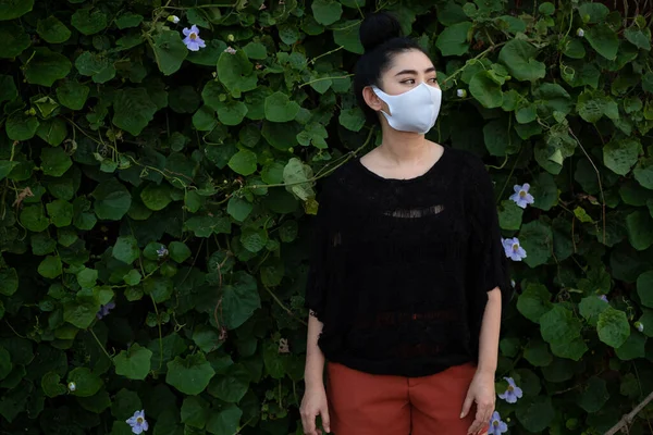 Portrait young Asia woman standing and putting on a fashion mask at leaf wall background with copy space