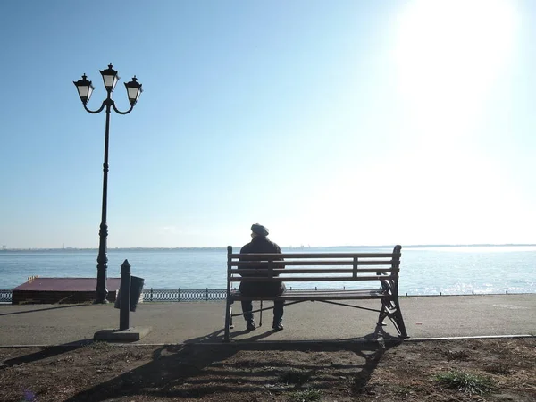 Starší muž sedí sám na lavičce opřený o hůl a dívá se do dálky a vzpomíná na své mládí — Stock fotografie