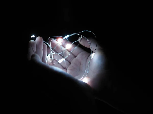 Luzes de Natal brilhando calorosamente closeup. Segurando guirlanda aconchegante em mãos . — Fotografia de Stock