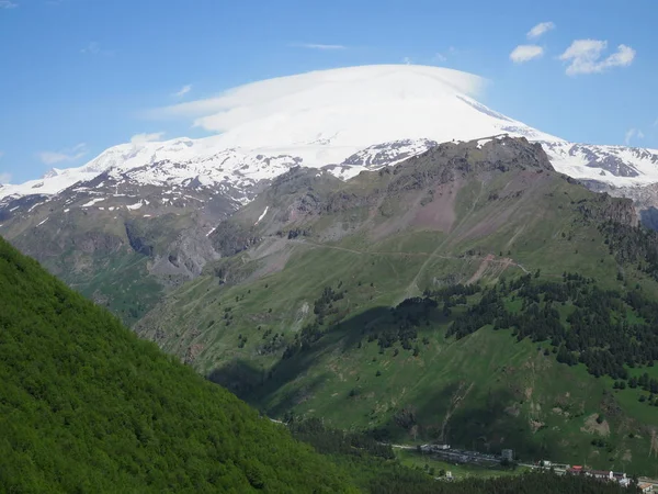Velká přírodní pohoří. Úžasná perspektiva kavkazské sněhové hory nebo sopky Elbrus se zelenými poli, modrá obloha pozadí. Elbrus pohled na krajinu-nejvyšší vrchol Ruska a Evropy — Stock fotografie
