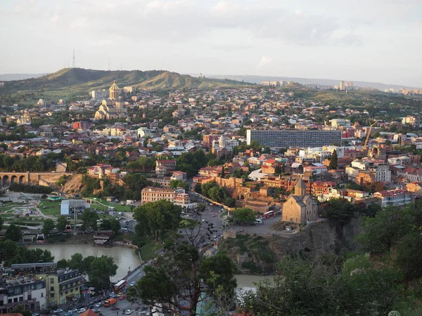 Luftaufnahme von der narikala-Festung auf der georgischen Hauptstadt Tiflis, voller kleiner Ziegeldachhäuser, grüner Bäume, Brücken über den Kura-Fluss. Georgien, Tiflis - Juni 2019 — Stockfoto