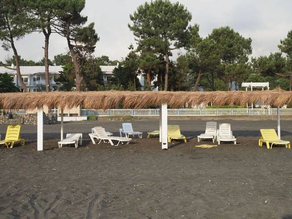 Sommer, Sonne, einsamer Strand an der Küste mit Liegestühlen. Strand am Meer mit leeren Liegestühlen in einer Reihe. menschenleere Unterkunft. verlassene Ferienanlage. Georgien, Ureki - Juni 2019 — Stockfoto