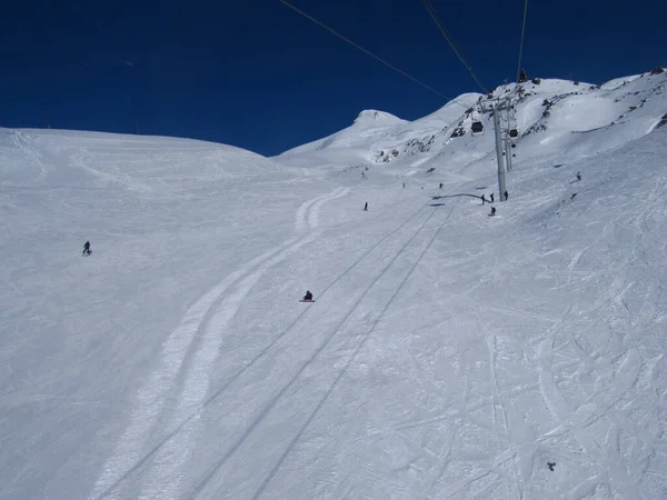 Freie Skipiste an einem klaren Wintertag, nur wenige Leute fahren, hinter sichtbaren Elbrus-Gipfeln. russland, elbrus region - februar 2010 — Stockfoto