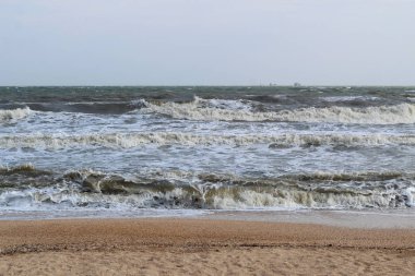 Denizde fırtına sırasında dalgalar. Uzakta büyük gemiler ve mavnalar görebilirsiniz.