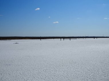 Tuz gölünün beyaz yüzeyi ve parlak mavi gökyüzü, insanlar uzaklarda yürüyor.