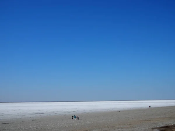 Superfície branca do lago de sal e o céu azul brilhante, pessoas andando na distância — Fotografia de Stock