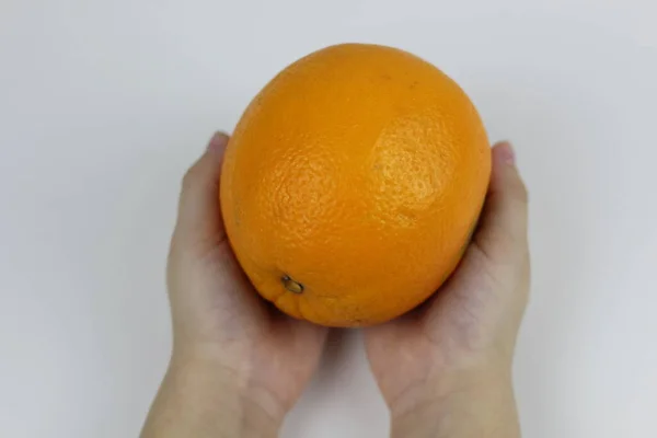 Руки ребенка держат спелый оранжевый на белом фоне — стоковое фото