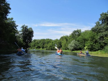 Güneşli bir günde bir grup turist kano üzerinde nehirde rafting yapıyor.