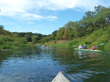 Bir grup insan dar bir nehirde kanolarla rafting yapıyor.
