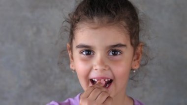 Süt dişini eliyle ve diliyle sallayan bir çocuğun portresi. Diş dilini sallıyor. Dişe eliyle dokunuyor. Dişsiz gülümseme. Kız kendi dişini çekmeye çalışıyor..
