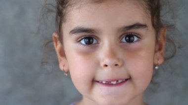 Süt dişini eliyle ve diliyle sallayan bir çocuğun portresi. Diş dilini sallıyor. Dişe eliyle dokunuyor. Dişsiz gülümseme. Kız kendi dişini çekmeye çalışıyor. Kapat.