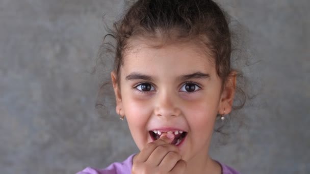 Portret van een kind dat een melktand schudt met zijn hand en tong. Schud een tand taal. Hij raakt de tand aan met zijn hand. Toothless glimlach. Het meisje probeert zelf een tand te trekken.. — Stockvideo