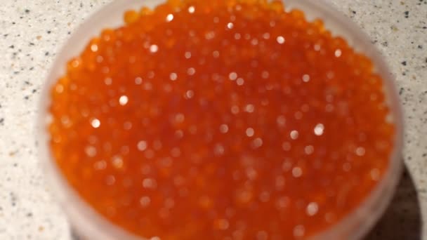 Verpackung roter Kaviar, der im Licht glänzt. Plastikgefäß mit rotem Kaviar von Meeresfischen. Geschenke des Meeres. Übergang vom Fokus zum scharfen Bild. eine leichte Bewegung des Rahmens. Nahaufnahme — Stockvideo