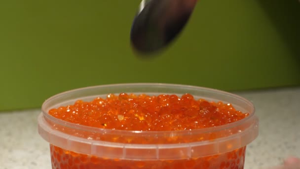 As mãos femininas recolhem uma colher de caviar do frasco. O caviar de salmão cai lindamente em um jarro. Frasco de plástico com caviar vermelho de peixe marinho. Presentes do mar. Fechar — Vídeo de Stock