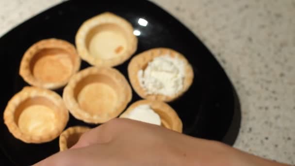 Frauenhände nehmen leere Törtchen von einem Teller und füllen sie mit Quark. Zubereitung von Snacks. Nahaufnahme — Stockvideo