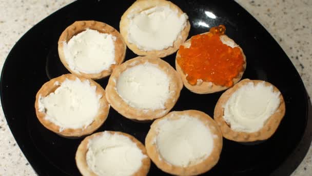 Rode kaviaar wordt met een lepel op taartjes met kwark gelegd. Bereiding van snacks met rode kaviaar. Bovenaanzicht. Sluiten. — Stockvideo