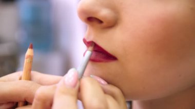 Makyöz genç bir kızın dudaklarını boyuyor. Dudaklarını fırçayla boya. Kırmızı renk. Makyaj sanatçısı genç kız için makyaj yapıyor, yakın plan..