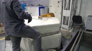 Bir işçi sertleştirici fırının kapısını açar. Çelik koğuşların söndürülmesi. Metal atölyesi.