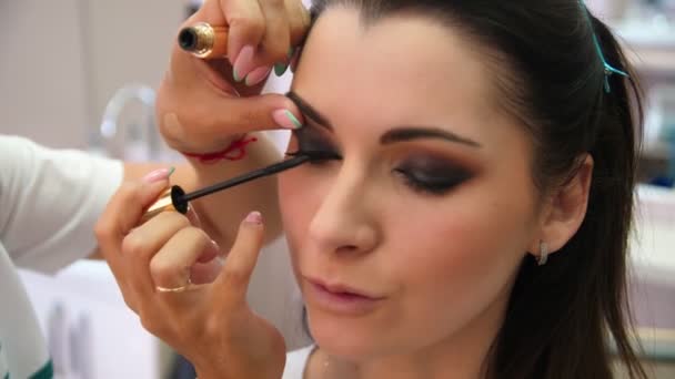 Make-up kunstenaar schildert de wimpers van een jonge vrouw. Make-up artiest doet make-up voor het jonge meisje, close-up. — Stockvideo