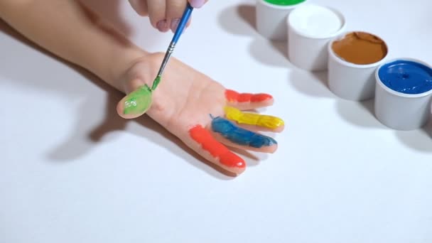 Een klein meisje tekent met gekleurde vingerverf op een wit papier — Stockvideo