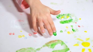 Küçük bir kız renkli parmaklarıyla beyaz bir kağıda resim çiziyor.