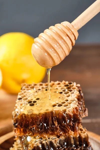fresh honey dripping from honey spoon to honey in honeycomb. lemon on the backboard