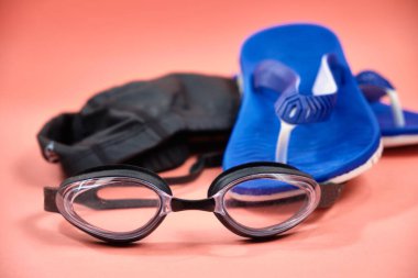 Accessories for swimming in the pool, glasses, cap, slates on a pink background